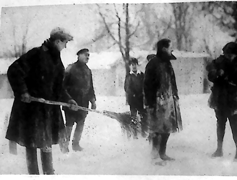 Stróż parkowy miotłą otrzepuje śnieg z ubrania przewróconego saneczkarza w warszawskim parku Agricola. Fotografia z 1926 r.