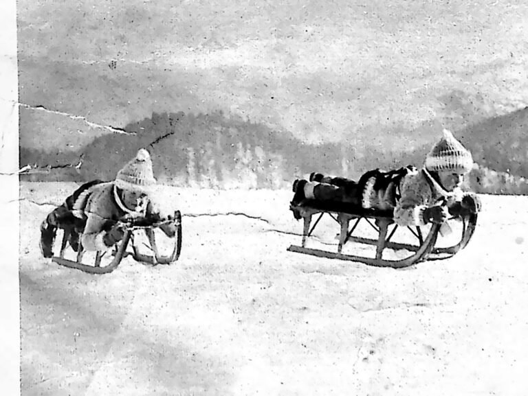 Dwoje małych dzieci w czapkach z pomponami na saneczkach na śniegu w St. Moritz. Fotografia z 1926 r.
