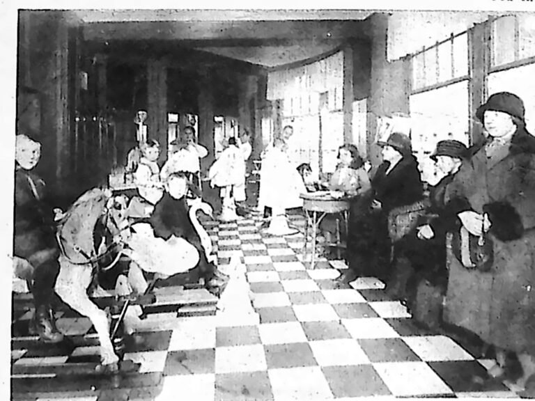 Wnętrze zakładu fryzjerskiego z szachownicową posadzką; dzieci bawią się na zabawkowych konikach, obok siedzą matki. Fotografia z 1926 r.