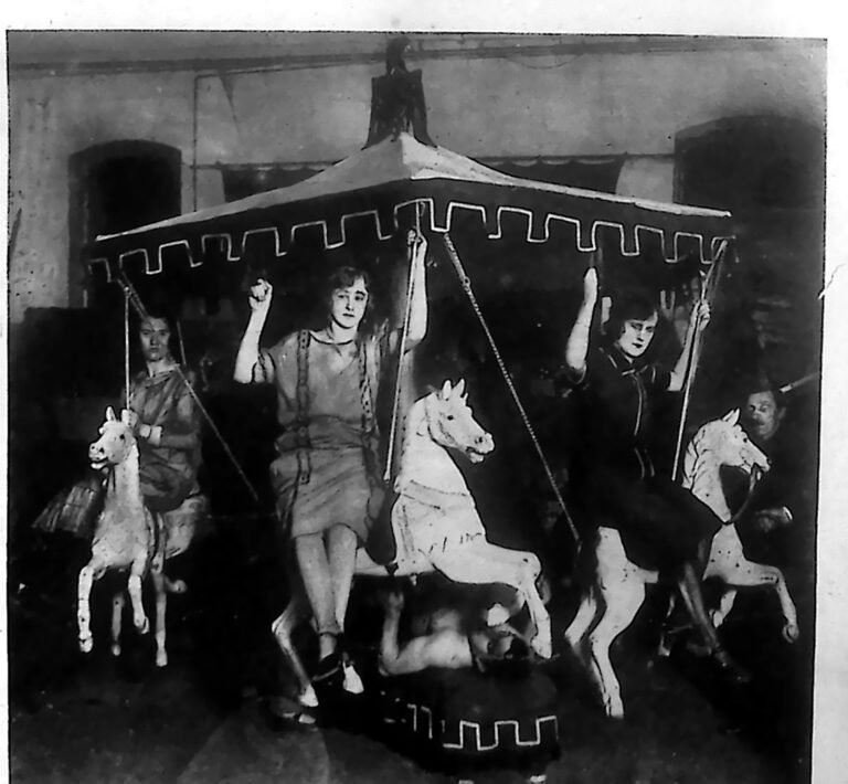 Siłacz dźwigający na sobie niewielką karuzelę z konikami, na których siedzą ludzie. Fotografia z 1926 r.