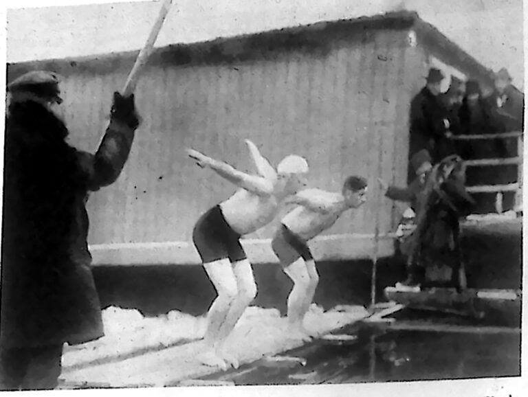 Dwaj pływacy na pomoście nad zimową Wisłą w chwili startu, wśród widzów w płaszczach. Fotografia z 1926 r.