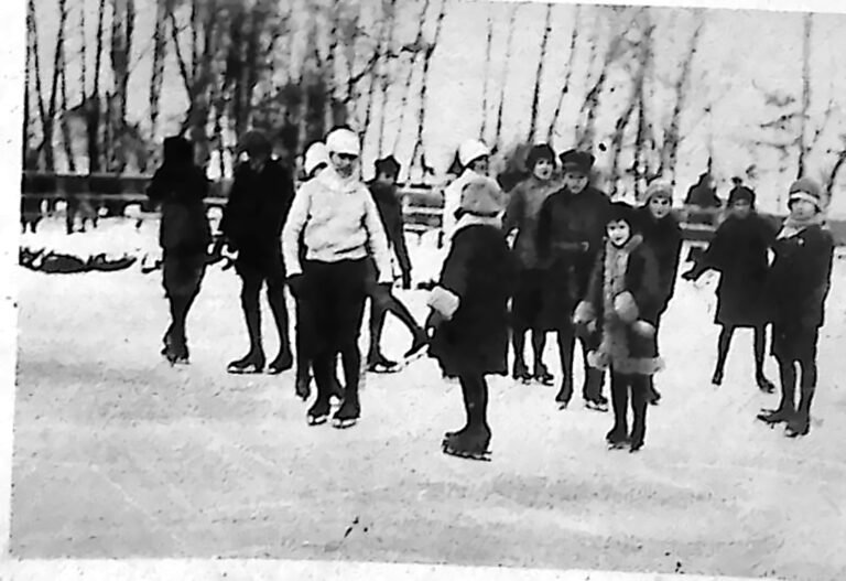 Grupa dzieci na łyżwach na torze łyżwiarskim w Parku Krakowskim, wśród bezlistnych drzew. Fotografia z 1926 r.