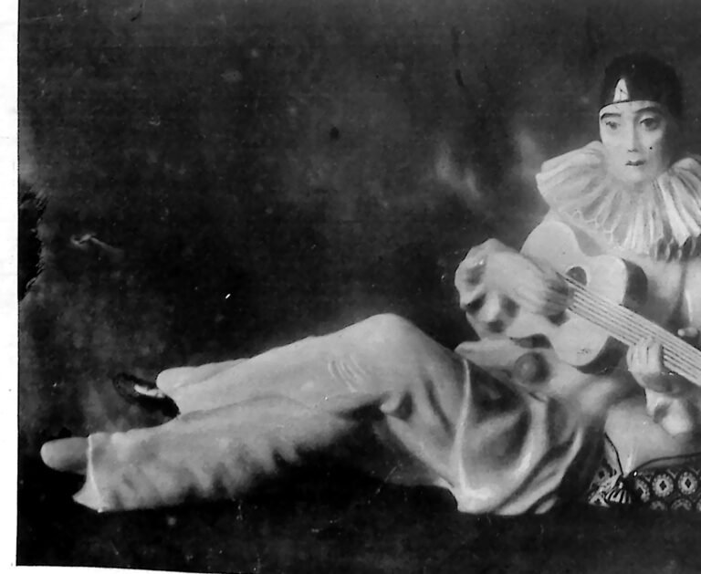 Porcelanowa figura leżącego Pierrota w kryzie, grającego na mandolinie, na ciemnym tle. Fotografia z 1926 r.