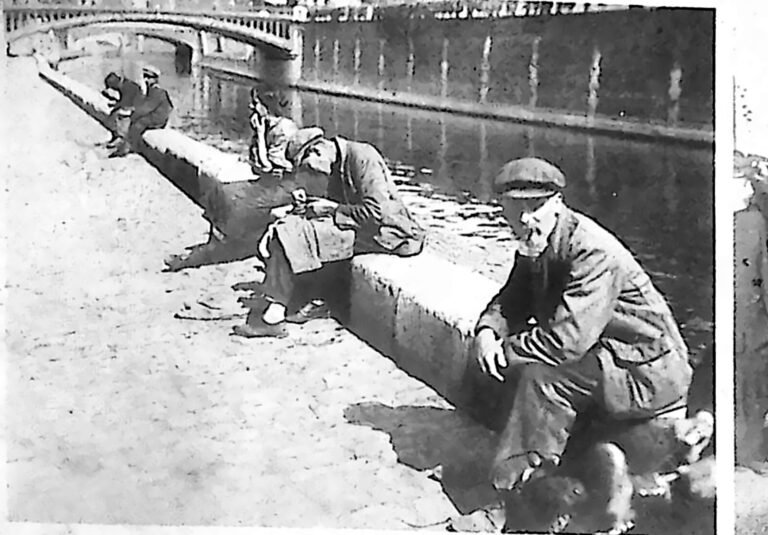 Mężczyźni siedzący i leżący na kamiennym nabrzeżu Sekwany pod mostem w Paryżu. Fotografia z 1926 r.