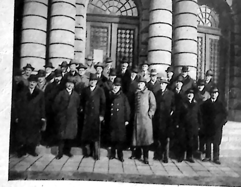 Grupa uczestników konferencji w paltach i kapeluszach przed kolumnadą gmachu Dyrekcji Kolei Państwowych w Poznaniu. Fotografia z 1926 r.
