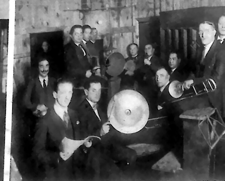 Muzycy zgromadzeni wokół wielkiego lejka nagraniowego w studio fonograficznym. Fotografia z 1926 r.