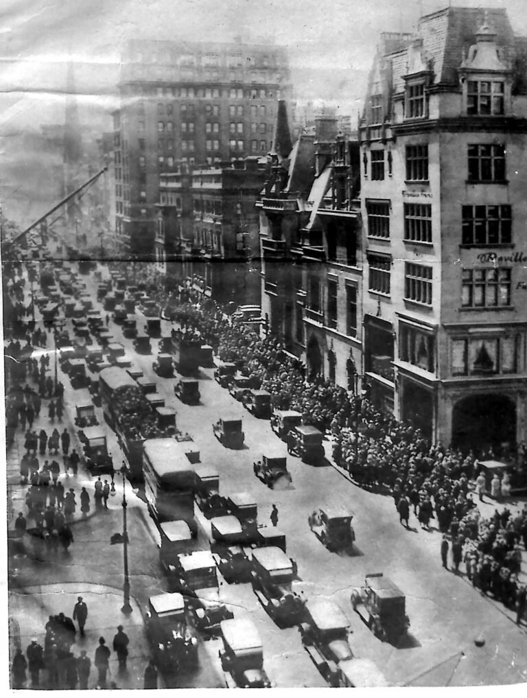 Widok z góry na zatłoczoną Park Avenue w Nowym Jorku: sznury samochodów i tłumy przechodniów między wysokimi kamienicami. Fotografia z 1926 r.