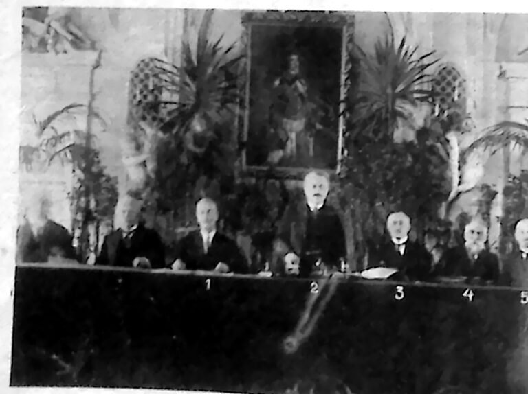 Prezydium zjazdu za długim stołem na tle palm w sali Rady Miejskiej w Warszawie. Fotografia z 1926 r.