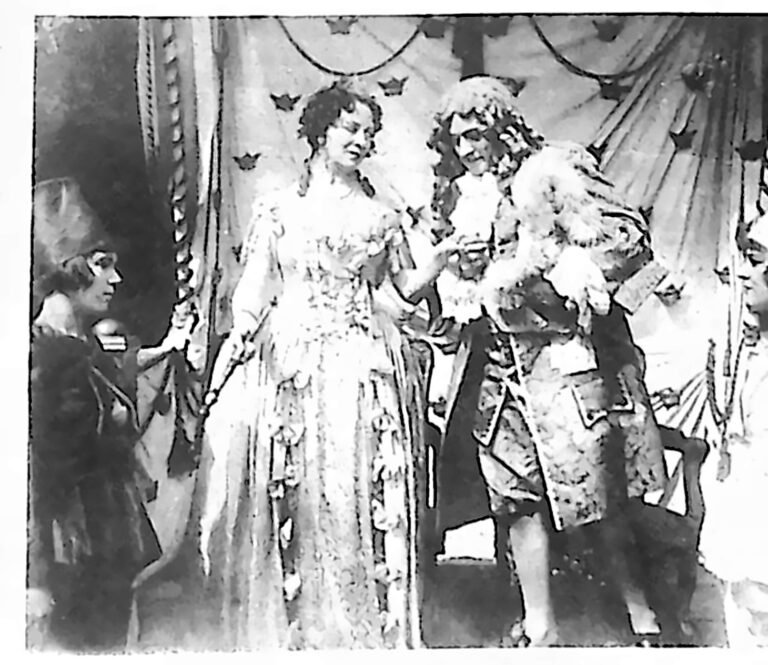 Scena kostiumowa z filmu: dama w sukni z epoki baroku w otoczeniu dworzan w perukach. Fotografia z 1926 r.