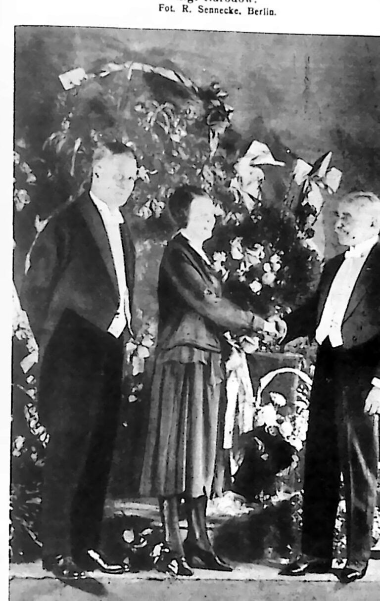 Młoda śpiewaczka z wielkim bukietem kwiatów przyjmująca gratulacje dwóch panów we frakach. Fotografia z 1926 r.