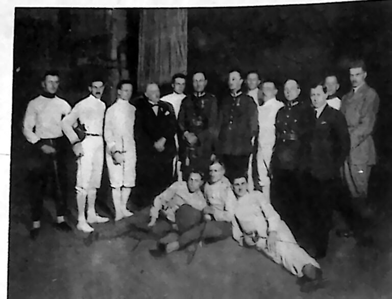 Szermierze w białych strojach i widzowie w mundurach, ustawieni do wspólnego zdjęcia w sali Apollo w Poznaniu. Fotografia z 1926 r.