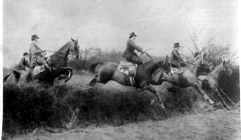 Trzy amazonki na koniach pokonujące żywopłotową przeszkodę podczas wyścigu w East Knoyle. Fotografia z 1926 r.