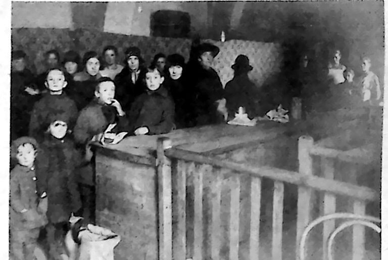 Dzieci i dorośli stojący w kolejce przy barierce po obiad w refektarzu klasztoru Franciszkanów w Krakowie. Fotografia z 1926 r.