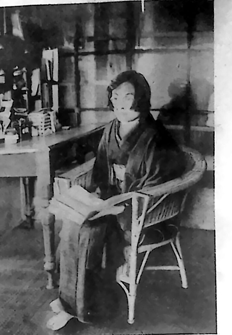 Japonka w kimonie siedząca w wiklinowym fotelu przy biurku z książką na kolanach. Fotografia z 1926 r.