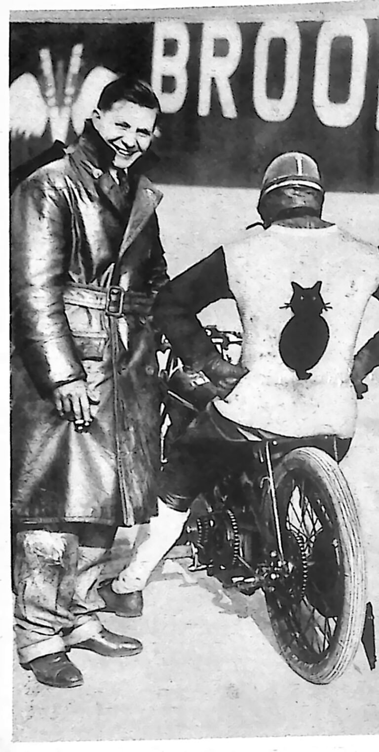 Motocyklista w kombinezonie z wyszytym czarnym kotem na plecach, obok mężczyzna w płaszczu przy motocyklu. Fotografia z 1926 r.