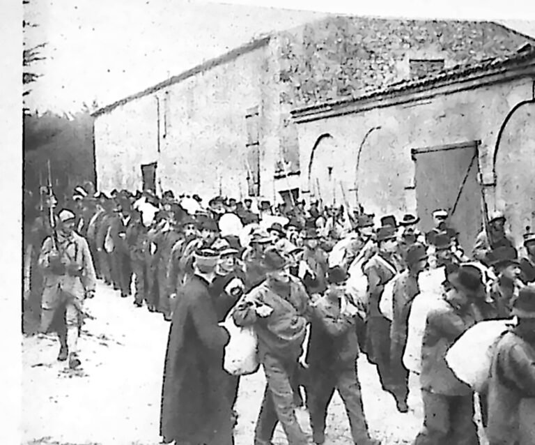 Długa kolumna skazańców z tobołkami, prowadzona przez żandarmów wzdłuż muru portowego. Fotografia z 1926 r.