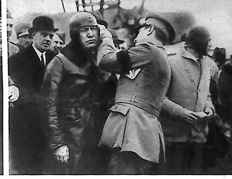 Mussolini w skórzanej kurtce i pilotce, ubierany przez oficera na lotnisku w Montecelio. Fotografia z 1926 r.