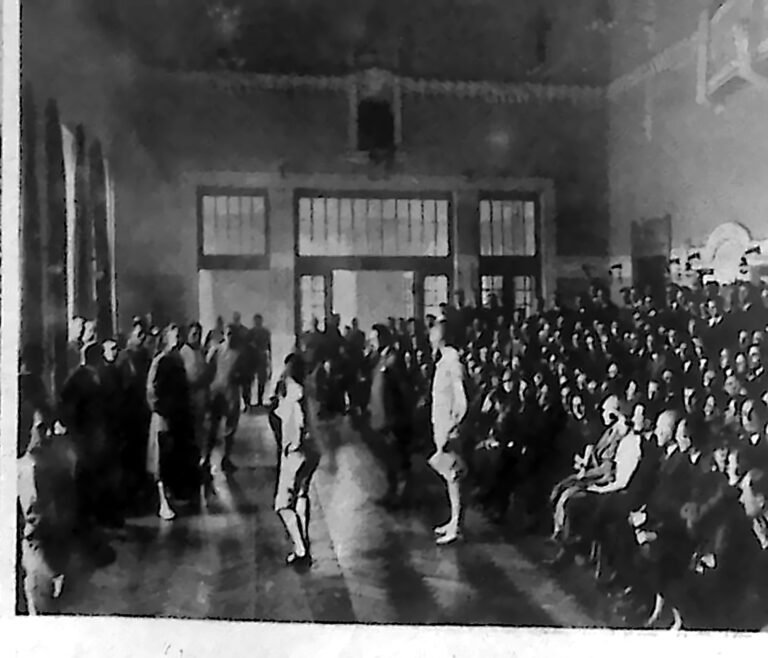 Dwaj szermierze w walce na szable na planszy w sali kasyna oficerskiego, wokół liczna publiczność. Fotografia z 1926 r.