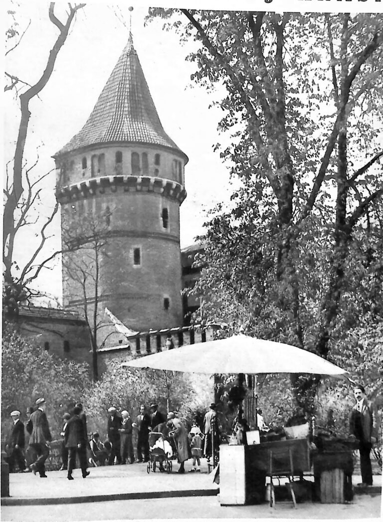 Baszta Stolarska na Plantach w Krakowie wśród rozwiniętych drzew; poniżej spacerowicze i wózek z parasolem. Fotografia z 1926 r.