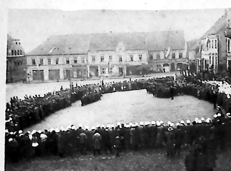 Owalny szpaler robotnic w białych czapeczkach ustawionych na rynku w Wodzisławiu. Fotografia z 1926 r.