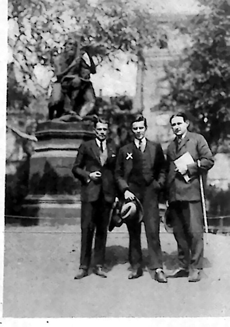 Trzej młodzi mężczyźni w garniturach przed pomnikiem na krakowskich Plantach. Fotografia z 1926 r.