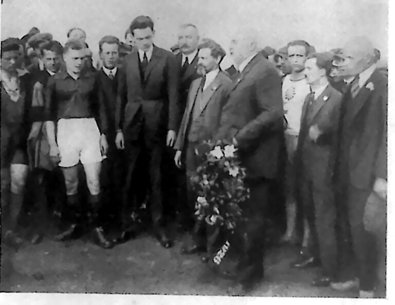 Piłkarze w strojach sportowych i działacze w garniturach z bukietem kwiatów na boisku. Fotografia z 1926 r.