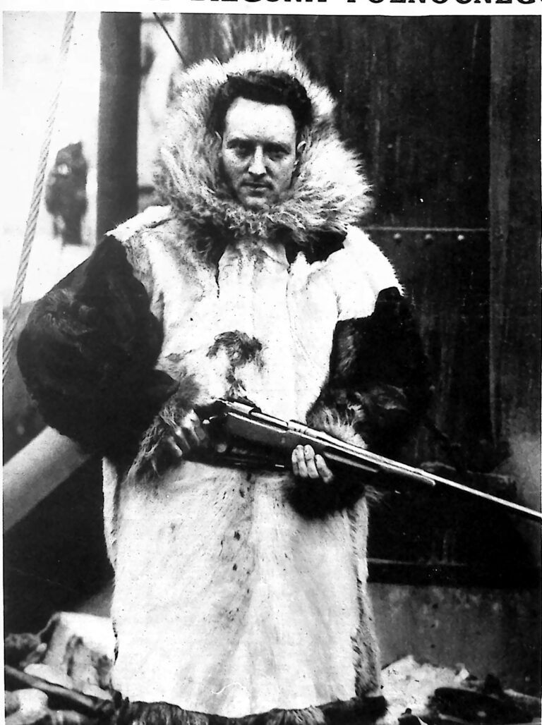 Richard Byrd w futrzanej parce z kapturem, ze strzelbą w rękach, na pokładzie statku. Fotografia z 1926 r.