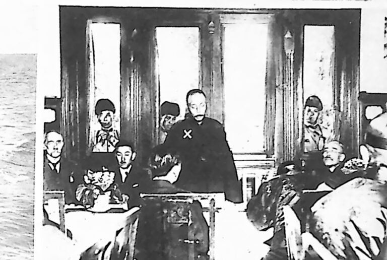 Generał w mundurze przemawiający do zgromadzonych dziennikarzy w wnętrzu z wysokimi oknami. Fotografia z 1926 r.